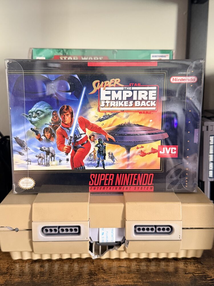A complete-in-box copy of Super Star Wars: The Empire Strikes Back for Super Nintendo, kept in a protective case on a SNES console